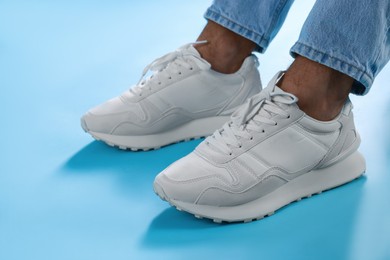 Man wearing stylish sneakers on light blue background, closeup