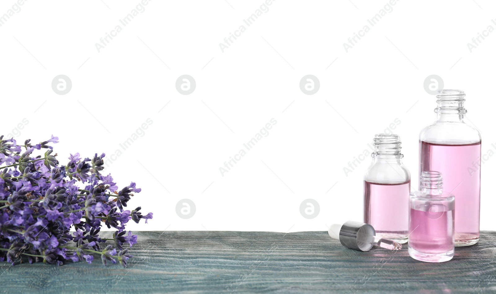 Photo of Bottles of essential oil and lavender flowers on blue wooden table against white background