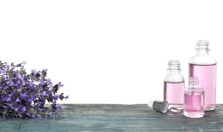 Photo of Bottles of essential oil and lavender flowers on blue wooden table against white background