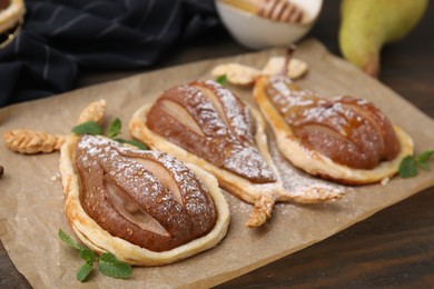 Delicious pears baked in puff pastry with powdered sugar and mint on wooden table, closeup