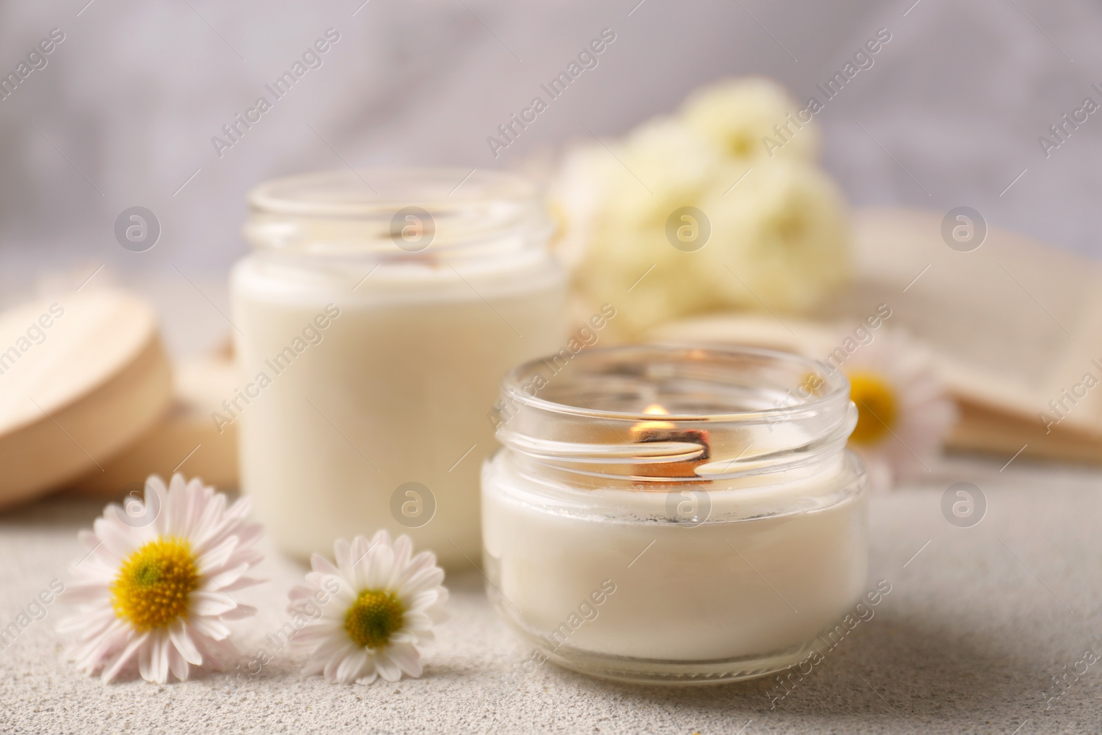 Photo of Burning scented candles and chamomile flowers on light gray textured table, closeup. Space for text