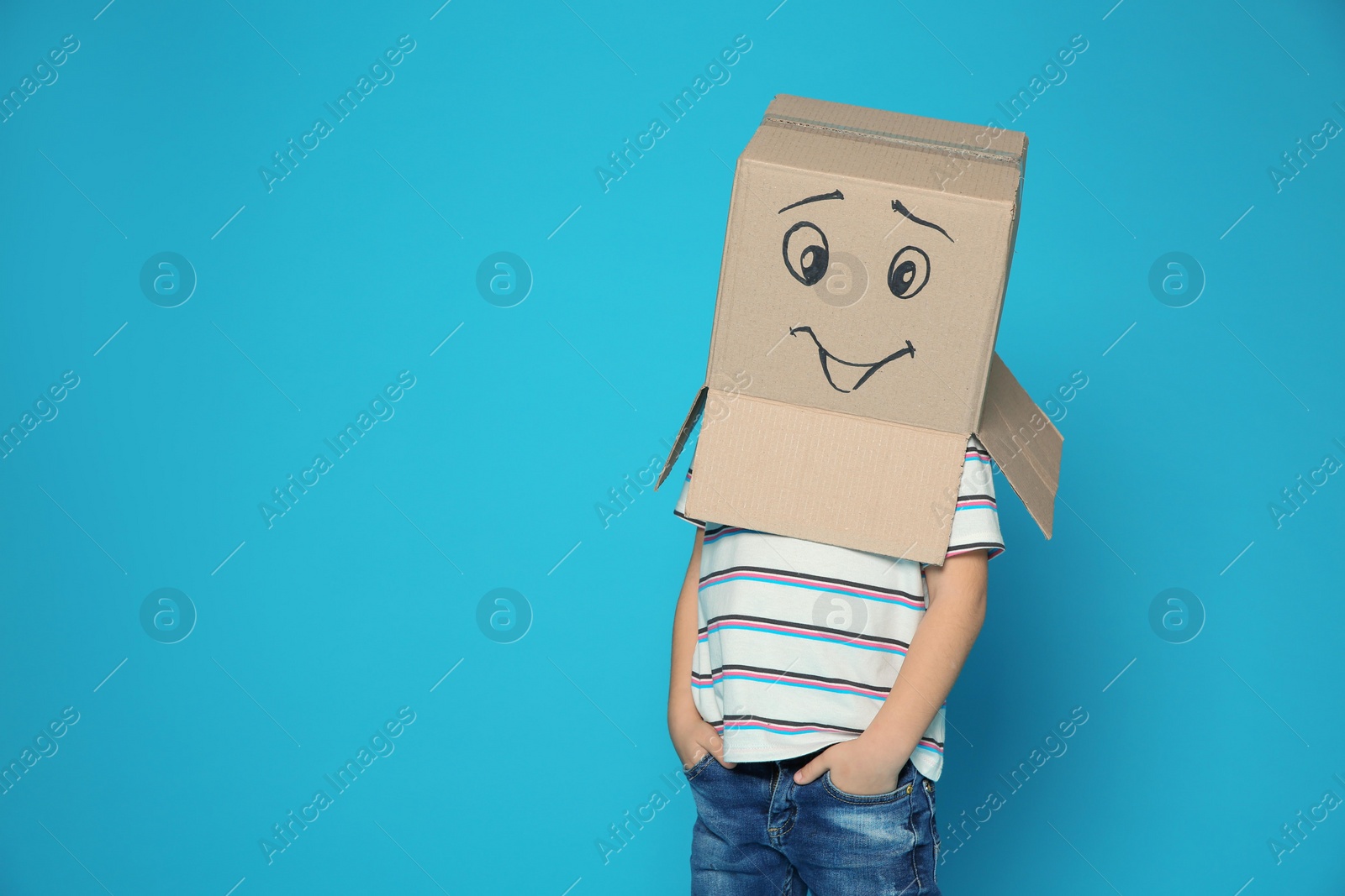 Photo of Cute little child wearing cardboard box with smiling face on color background. Space for text