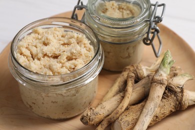 Photo of Tasty prepared horseradish and roots on wooden platter, closeup