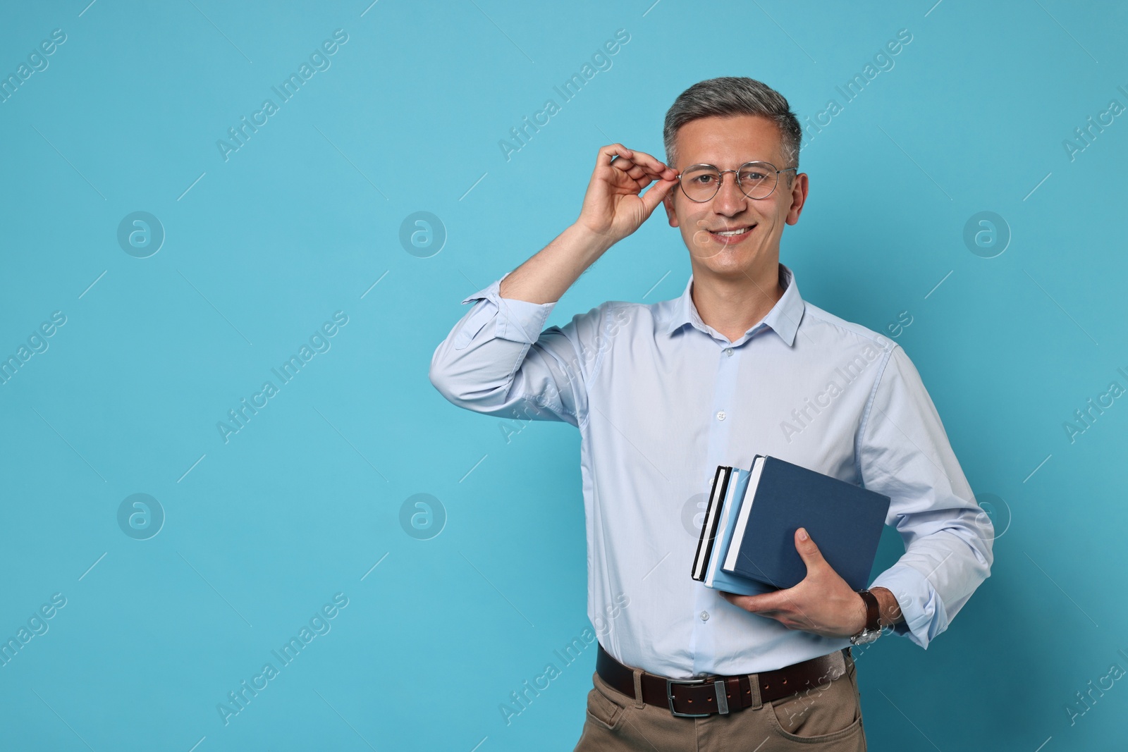 Photo of Teacher in glasses holding books on light blue background, space for text