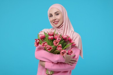 Photo of Happy woman in hijab with beautiful bouquet on light blue background