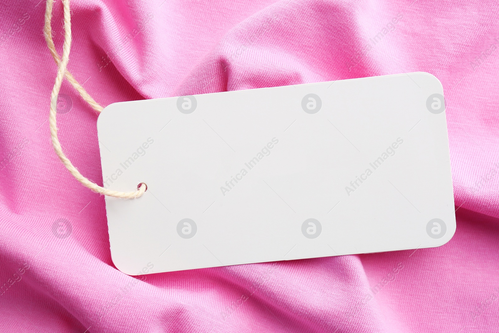 Photo of Cardboard tag with space for text on pink fabric, top view