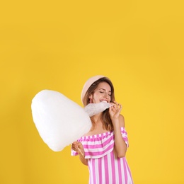 Happy young woman eating cotton candy on yellow background