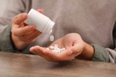 Photo of Man pouring antidepressants from bottle at wooden table, closeup