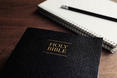 Photo of Holy Bible and notebook with pencil on wooden table, closeup. Religious book