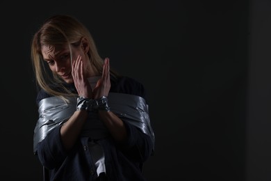 Photo of Scared woman taped up and taken hostage on dark background. Space for text