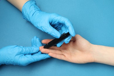 Diabetes. glucose testing. Doctor using lancet pen on blue background, closeup