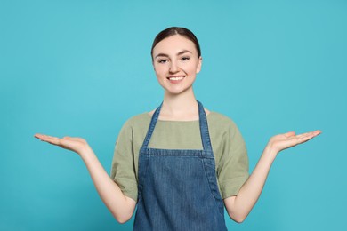 Beautiful young woman in clean denim apron on light blue background