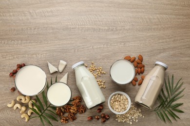 Photo of Different vegan milks and ingredients on wooden table, flat lay. Space for text