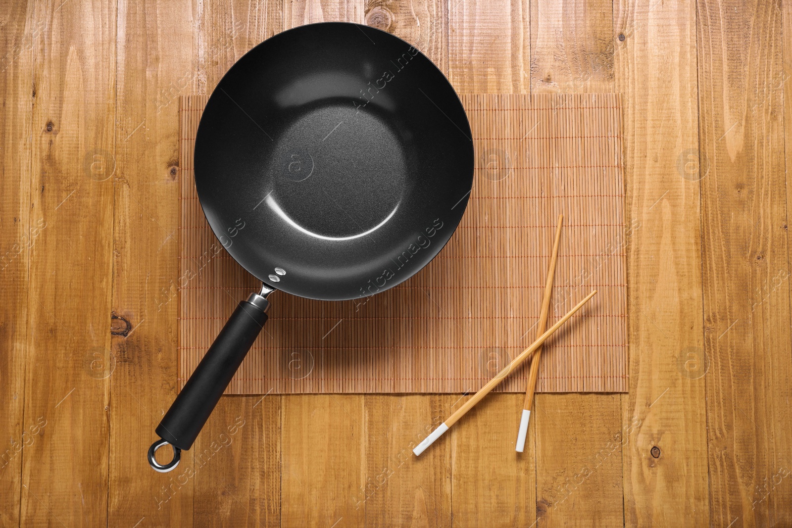 Photo of Empty iron wok and chopsticks on wooden table, top view