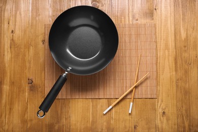 Empty iron wok and chopsticks on wooden table, top view