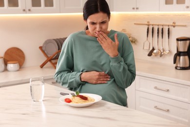 Photo of Young woman feeling nausea while seeing food at table in kitchen. Toxicosis during pregnancy