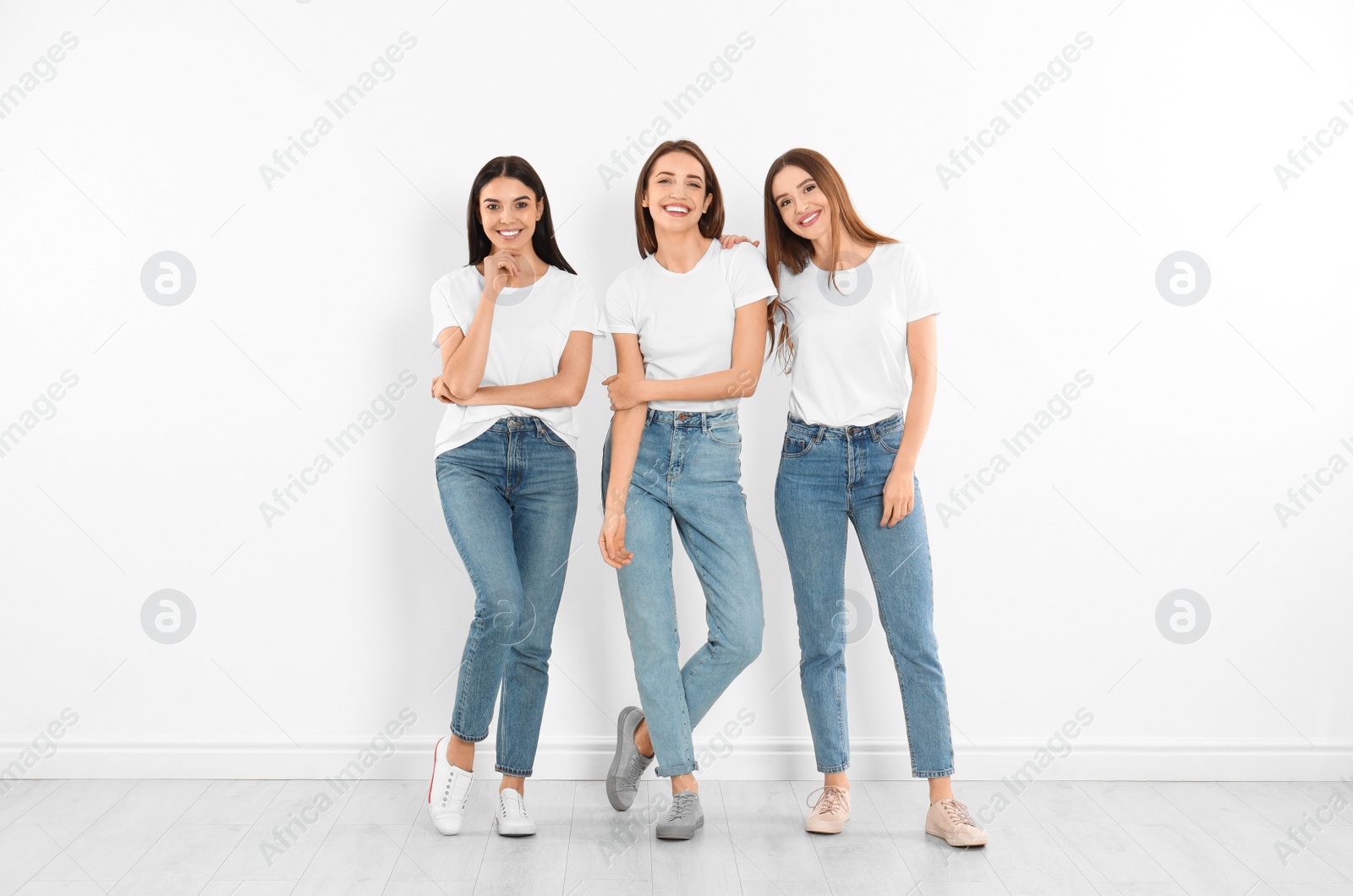 Photo of Group of young women in stylish jeans near white wall