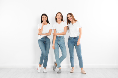 Photo of Group of young women in stylish jeans near white wall