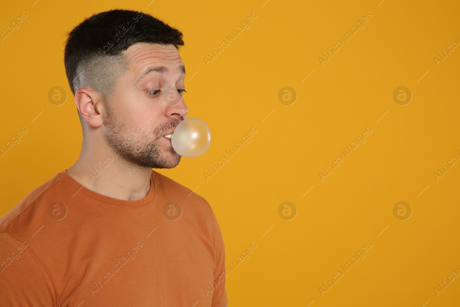 Photo of Surprised man blowing bubble gum on orange background, space for text
