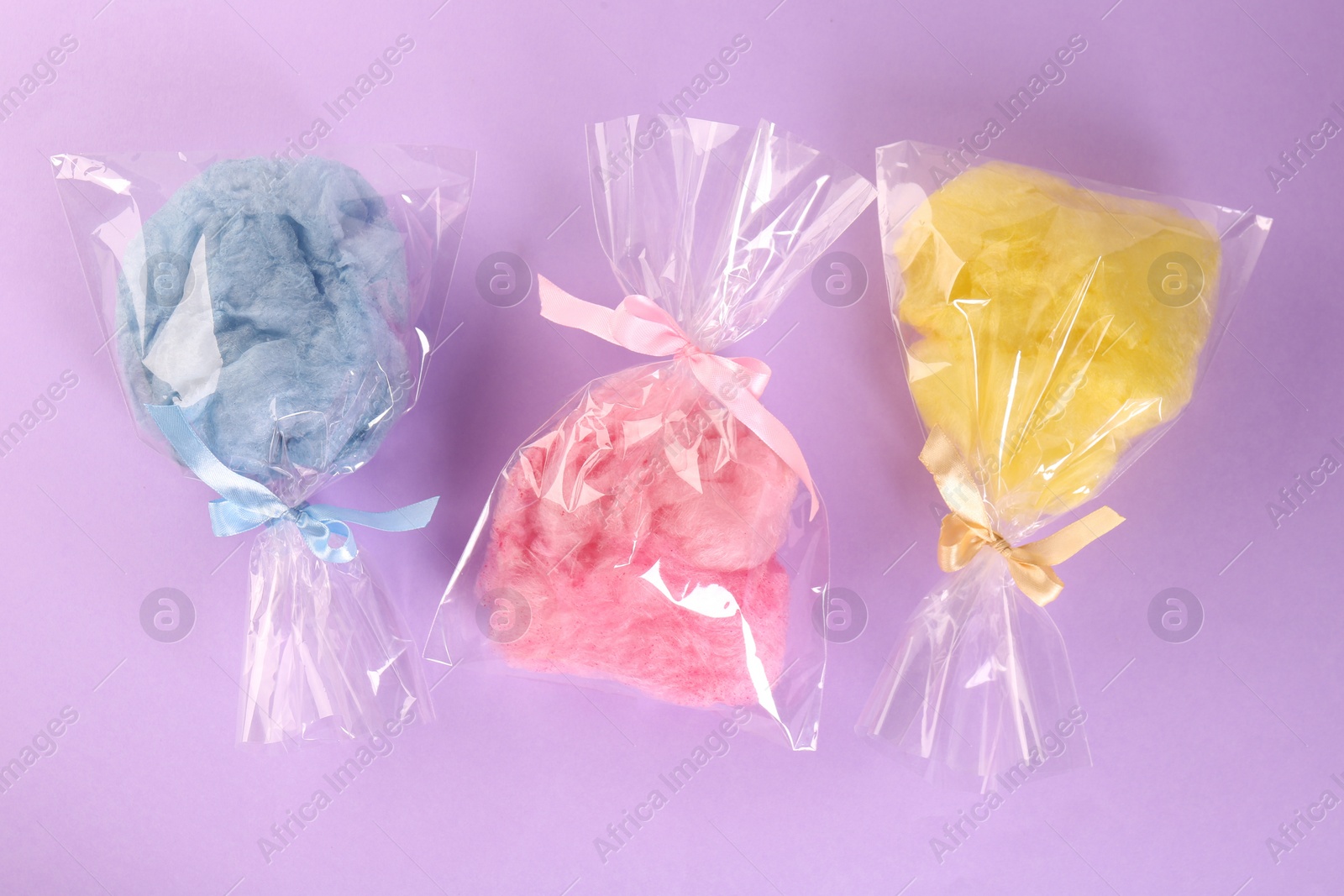 Photo of Packaged sweet cotton candies on violet background, flat lay