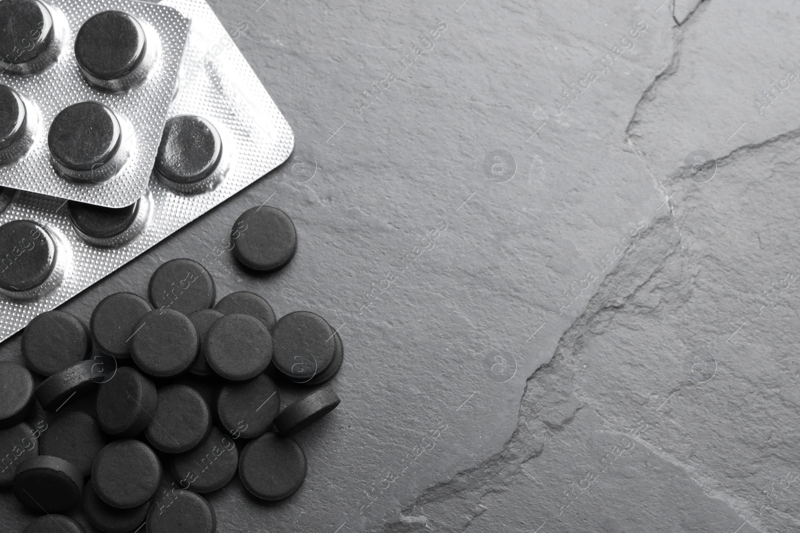 Photo of Activated charcoal pills and space for text on black table, flat lay. Potent sorbent