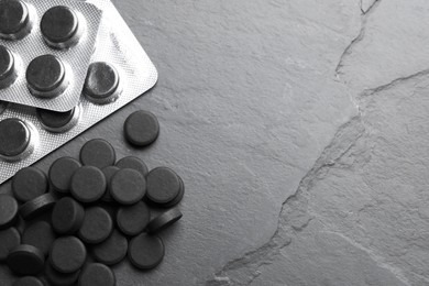 Photo of Activated charcoal pills and space for text on black table, flat lay. Potent sorbent