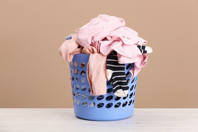 Photo of Plastic laundry basket with clothes near beige wall