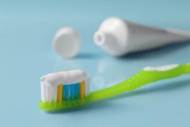Photo of Green brush with toothpaste on light blue background, closeup