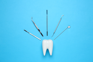 Photo of Ceramic model of tooth and dentist tools on light blue background, flat lay