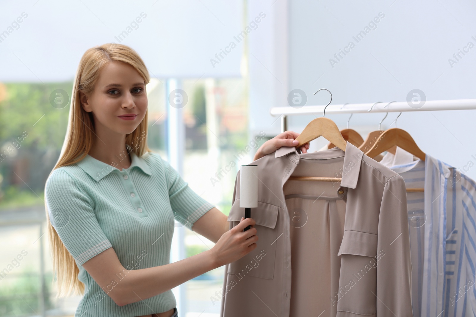 Photo of Young woman cleaning clothes with lint roller indoors