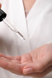 Photo of Woman applying cosmetic serum onto hand, closeup