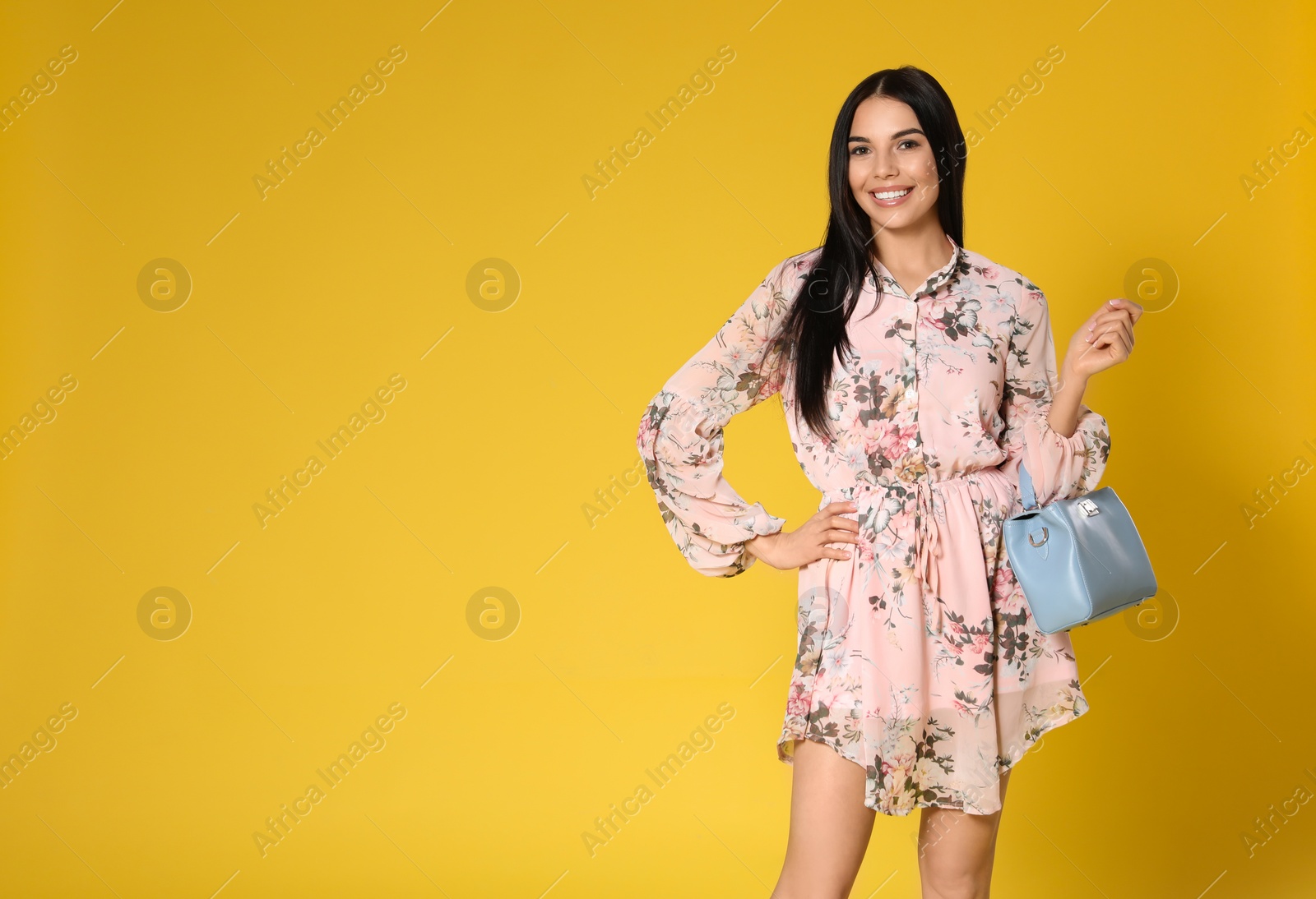 Photo of Young woman wearing floral print dress with stylish handbag on yellow background. Space for text