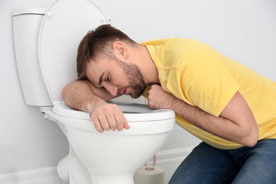 Photo of Young man suffering from nausea over toilet bowl indoors