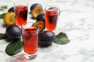 Photo of Delicious plum liquor and ripe fruits on white table. Homemade strong alcoholic beverage