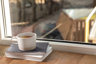 Cup of winter drink and books on windowsill. Space for text