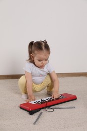 Photo of Cute little girl playing with toy piano at home