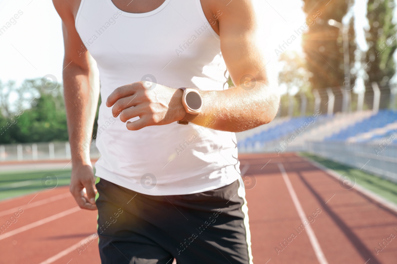 Photo of Man with fitness tracker running at stadium, closeup