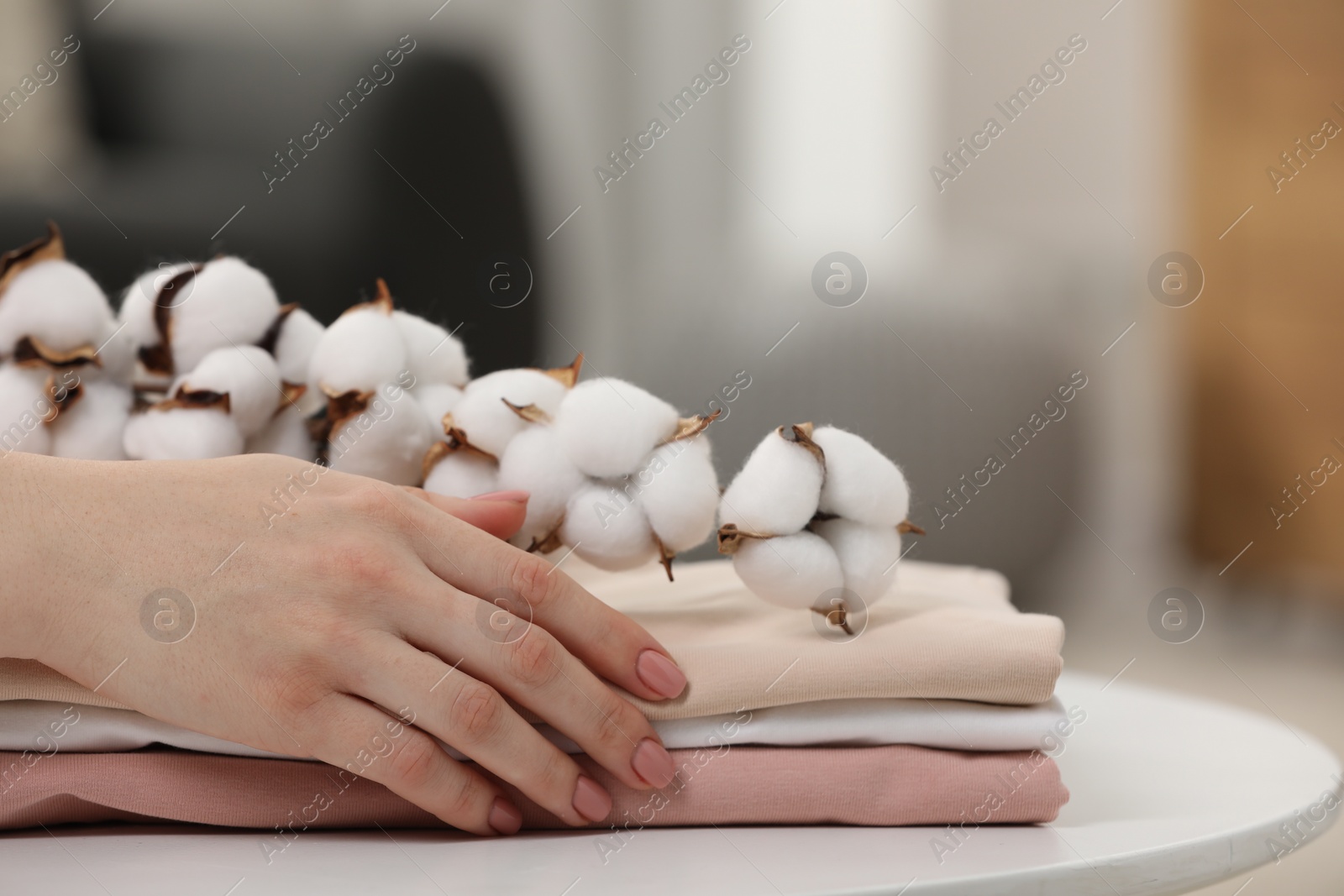 Photo of Woman touching bed sheets and cotton branch with fluffy flowers at white table in room, closeup