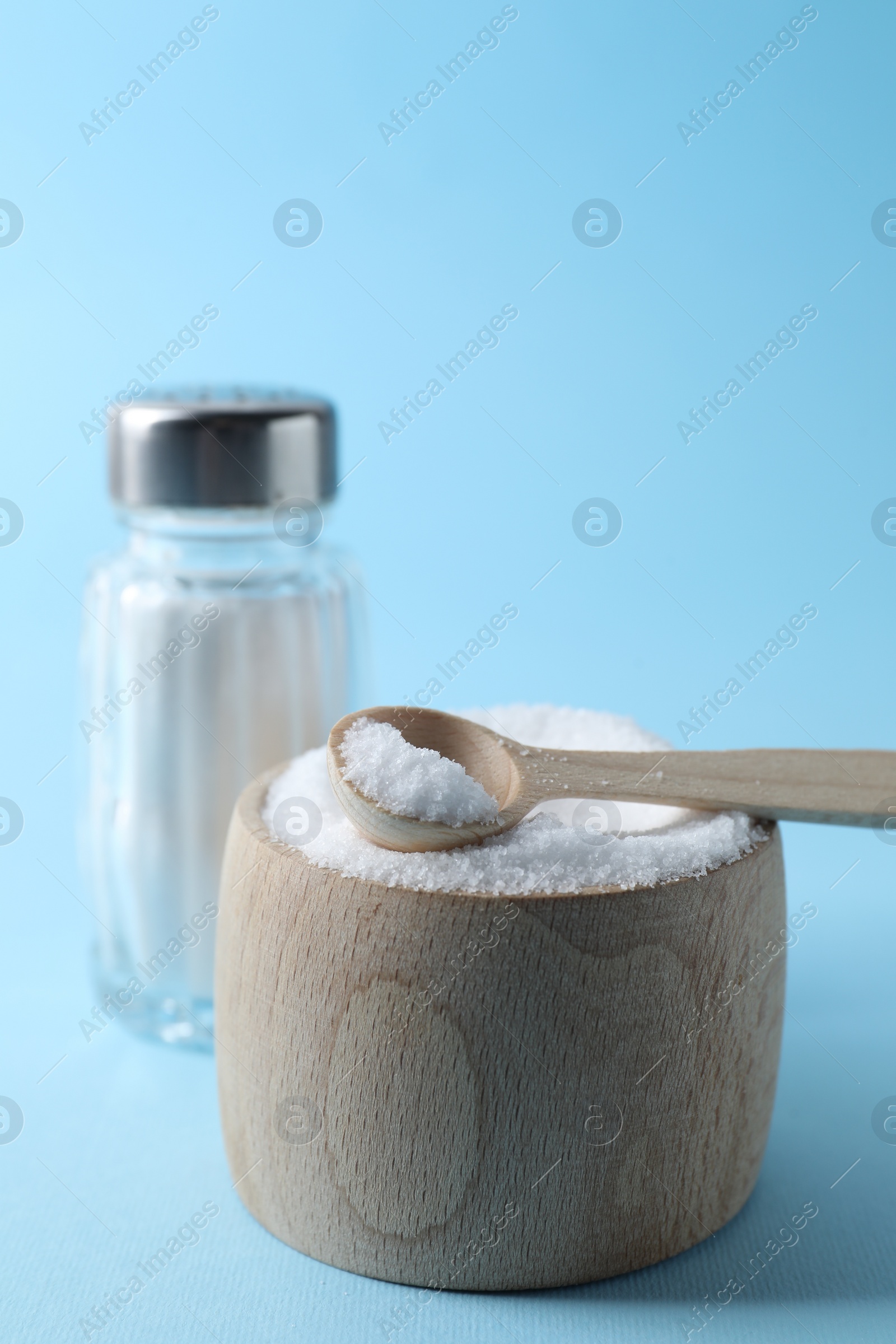 Photo of Organic white salt in bowl and shaker on light blue background