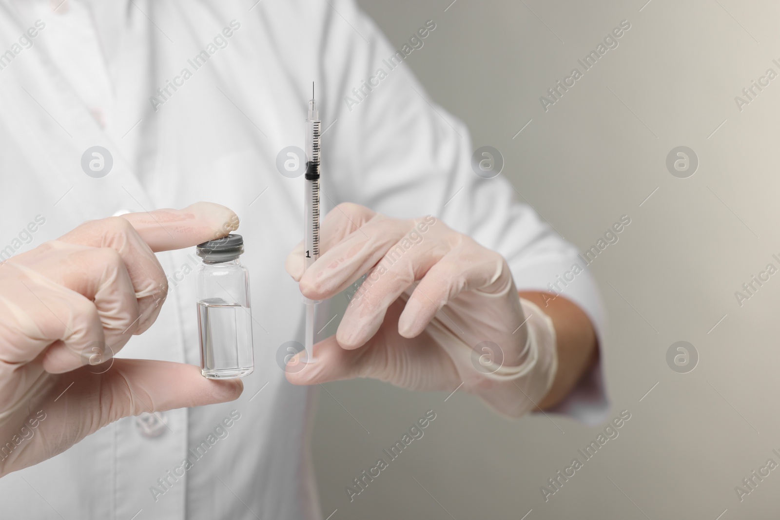 Photo of Doctor holding syringe and glass vial on grey background, closeup. Space for text