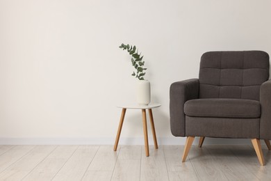 Photo of Comfortable armchair, side table and eucalyptus near white wall indoors, space for text