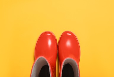 Photo of Red rubber boots on orange background, top view
