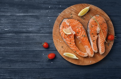 Photo of Board with fresh raw salmon steaks and seasonings on wooden background, top view