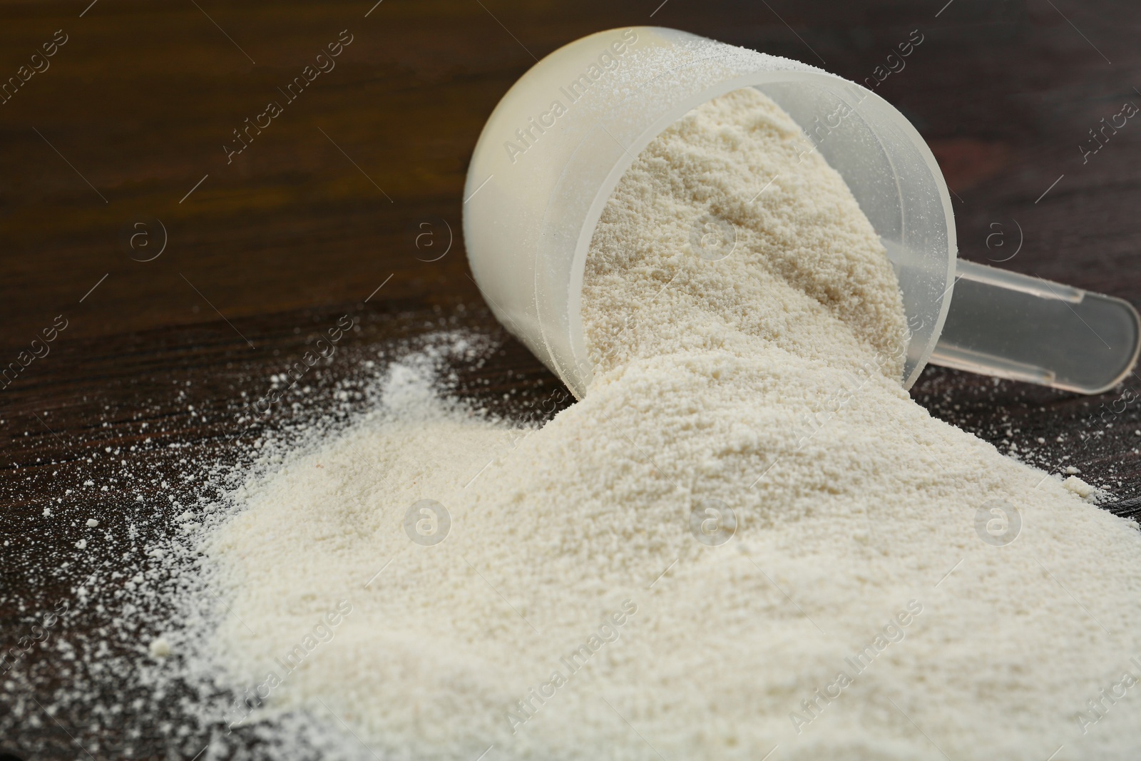 Photo of Overturned measuring scoop with protein powder on wooden table, closeup