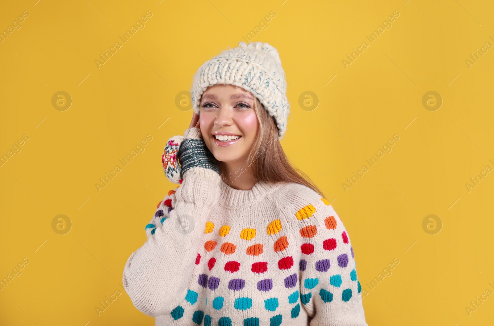 Photo of Young woman in warm sweater, mittens and hat on yellow background. Winter season