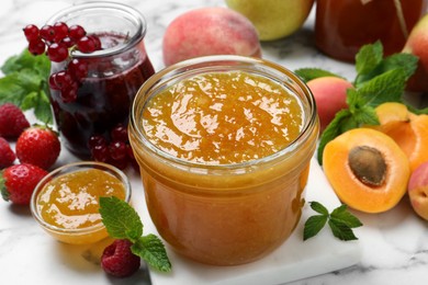 Photo of Jars with different jams and fresh fruits on white marble table, closeup