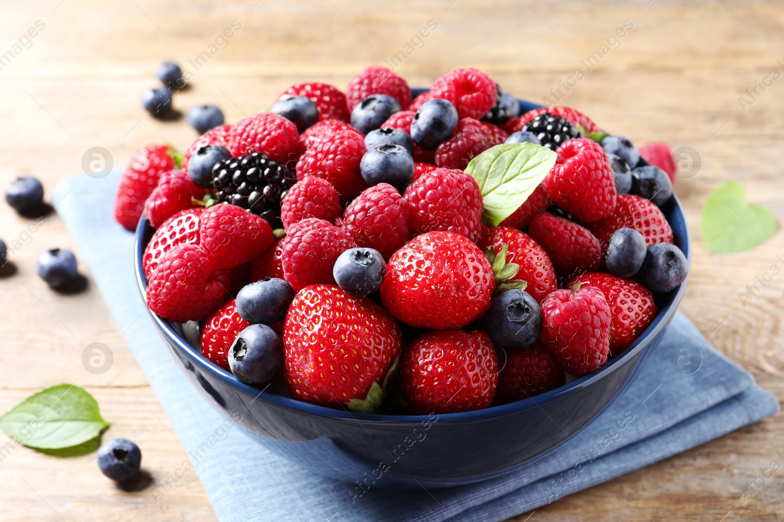 Photo of Different fresh ripe berries in bowl on wooden table, closeup