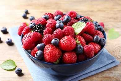 Photo of Different fresh ripe berries in bowl on wooden table, closeup