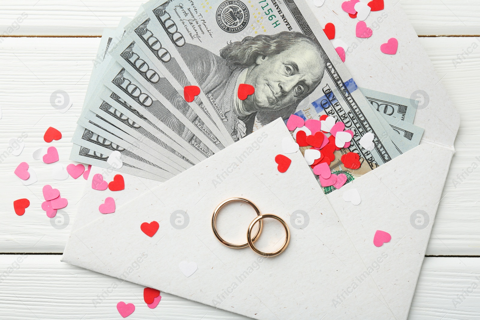 Photo of Honeymoon concept. Two golden rings, money and cutout hearts on white wooden table, flat lay