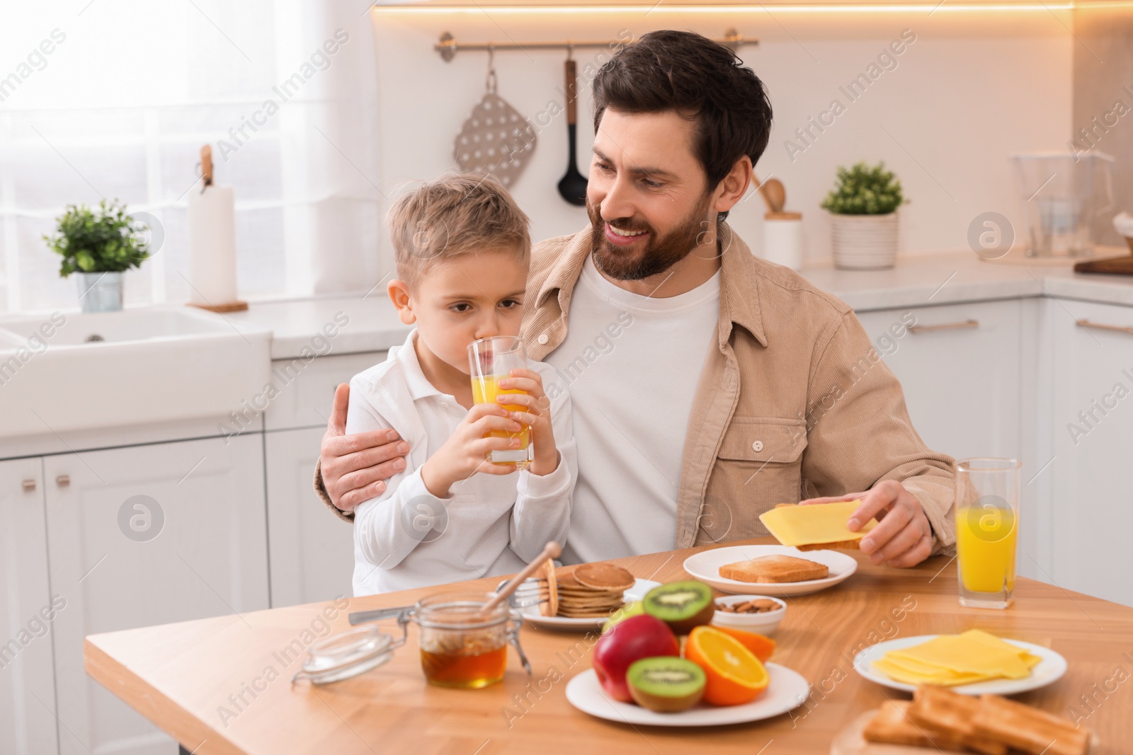 Photo of Father and his cute little son having breakfast at table in kitchen